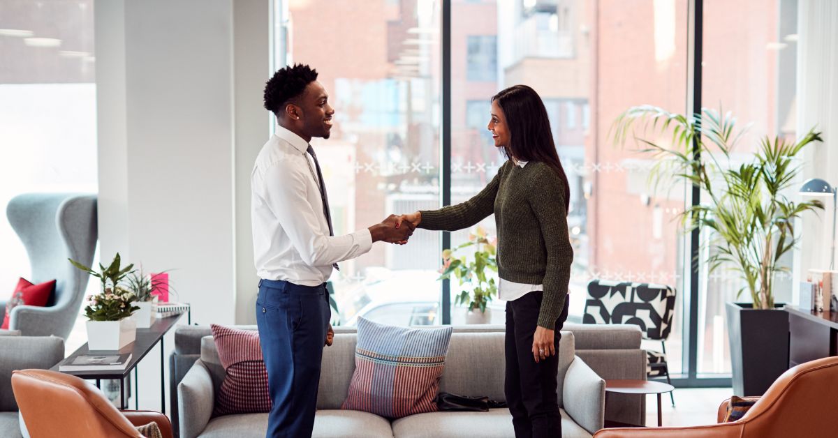 A man in a tie shakes hands with a woman in a sweater in a cozy looking office space