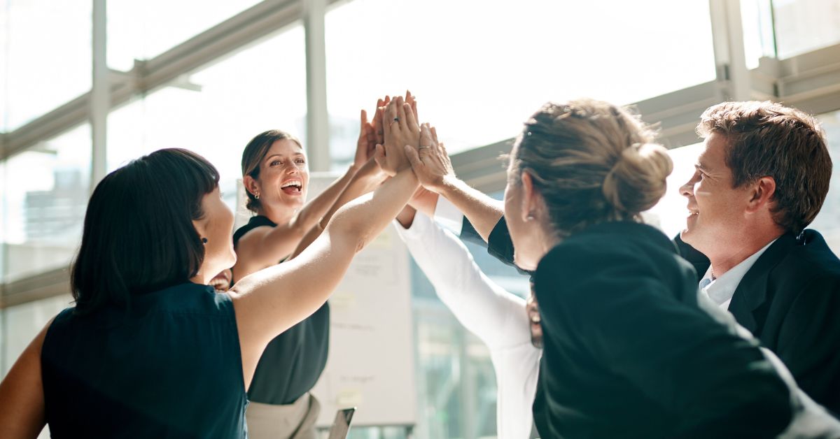 A group of young professionals all stand to do a 6-person high five in a well-lit office, employee recruitment strategies
